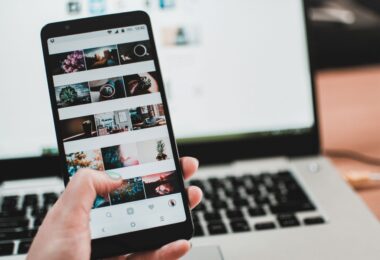 Person browsing social media on a phone in front of a laptop, switching to Instagram on PC