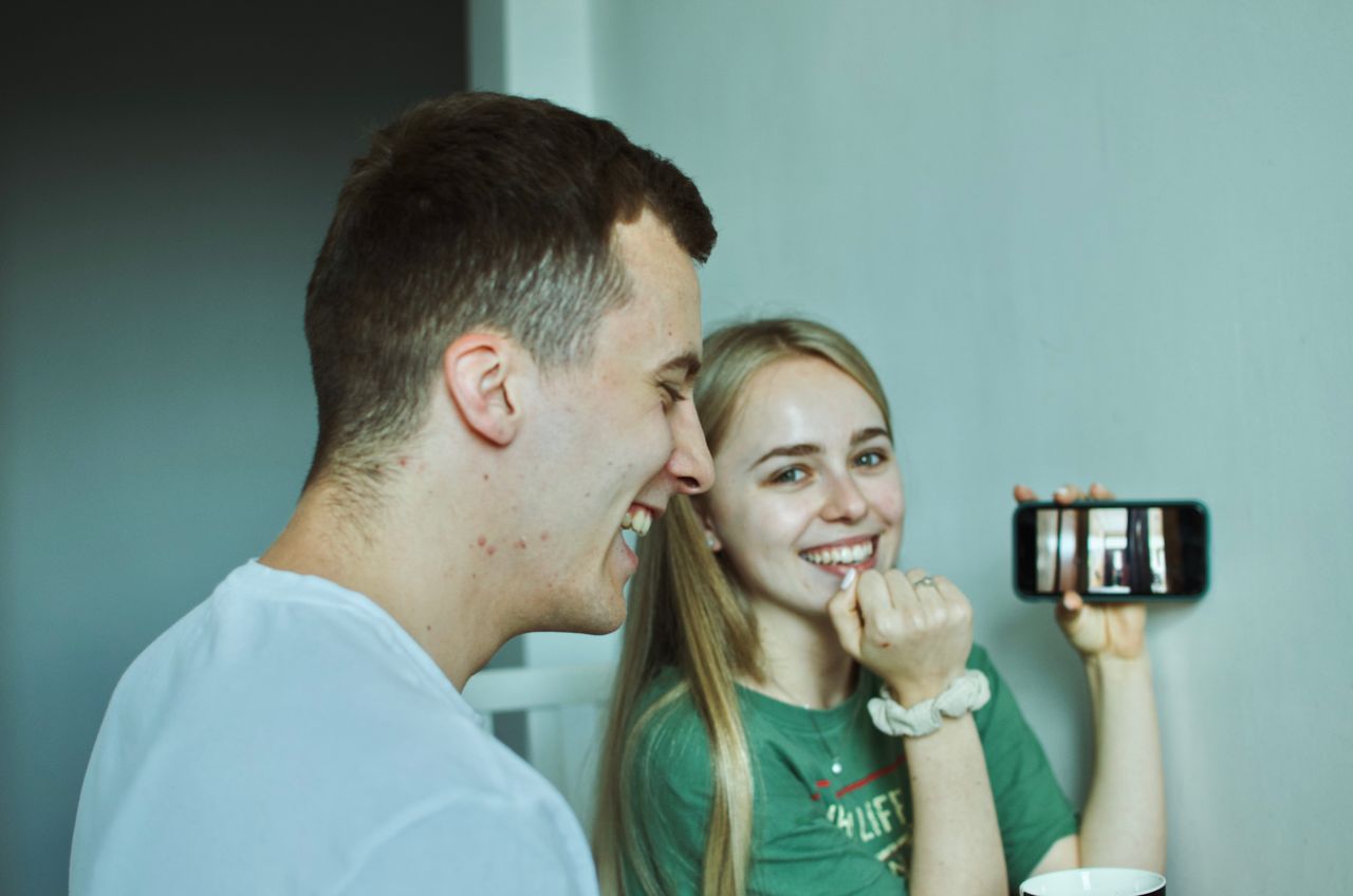 Two friends laughing while watching a saved video on a smartphone, an alternative to an online video downloader