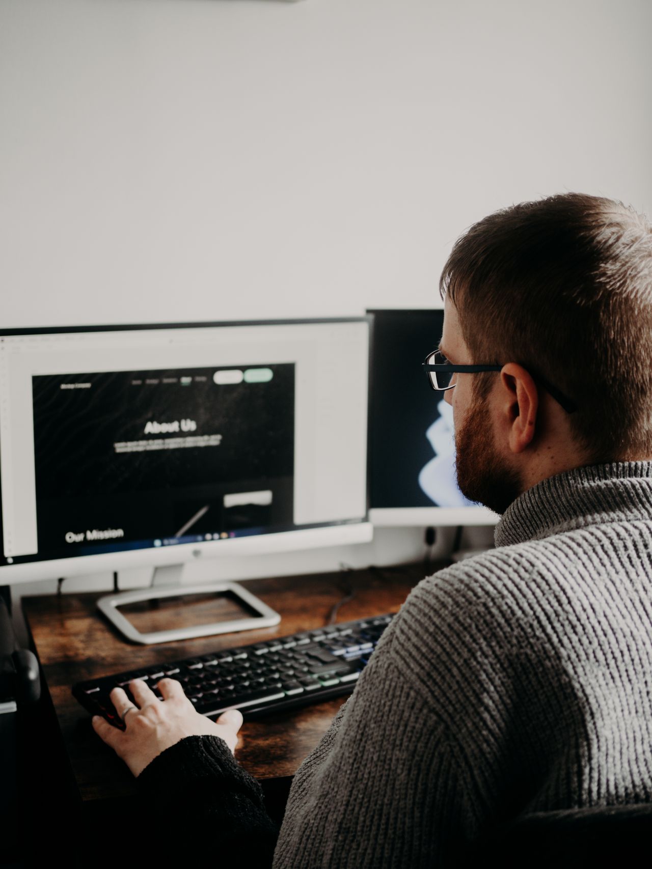 Man designing a website on dual monitors at a home office using a website builder