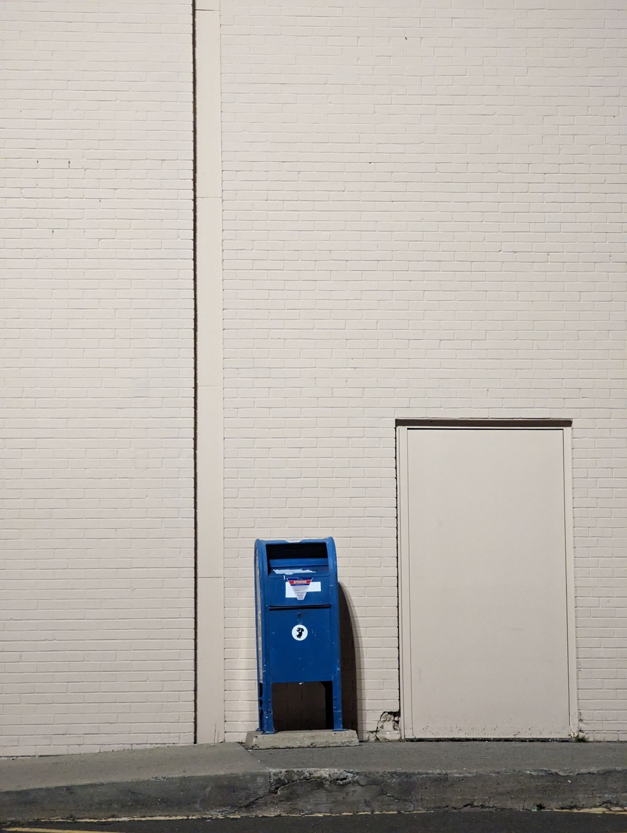 Blue USPS collection box beside a brick wall, a drop off point for prepaid label packages that fit
