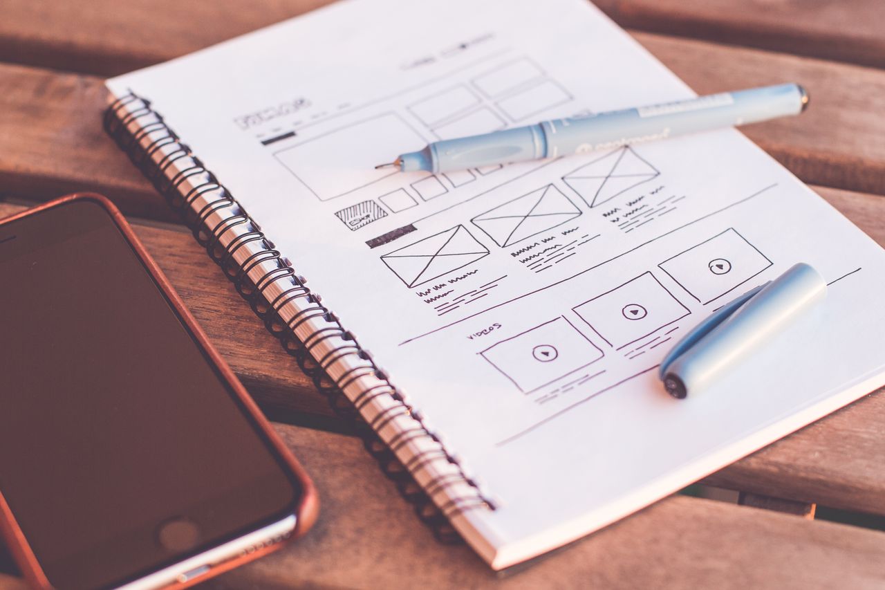 Website wireframe sketched in a notebook next to a phone, planning a site before choosing the best website builder