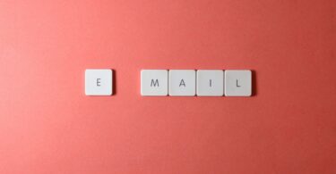 Keyboard letter tiles spelling email on a coral background, for a Benchmark Email review