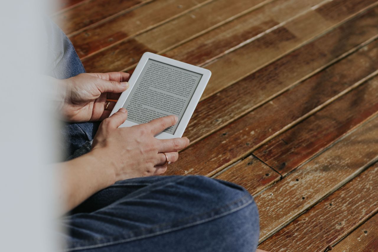 Hands holding an e-reader on a wooden floor, an example of ebook sales through SendOwl