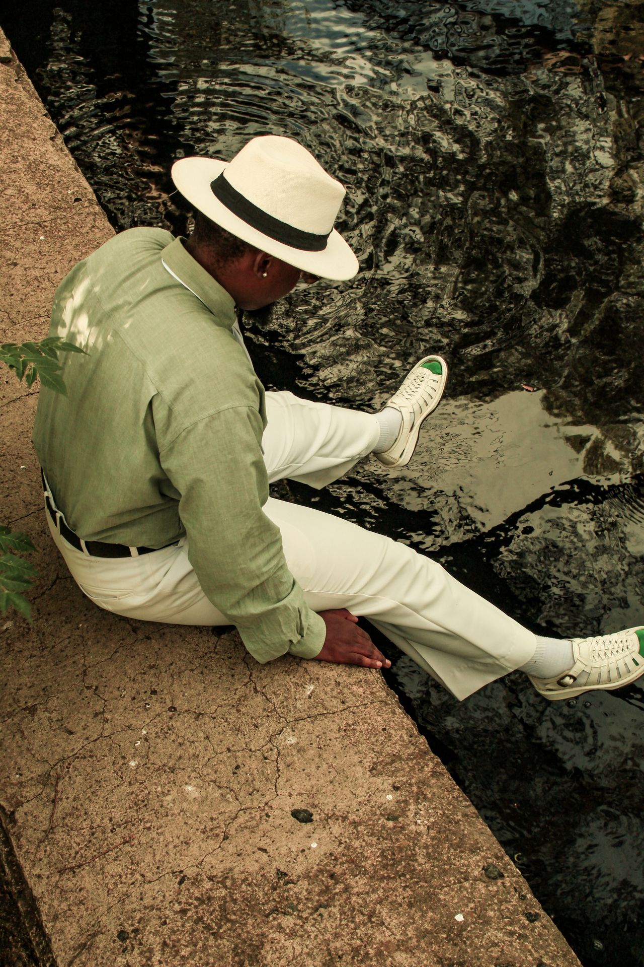 Man in a hat and green shirt relaxing by the water, a simple way to wear color in menswear