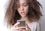 Surprised young woman looking at her phone, checking if online money earning sites are genuine or fake