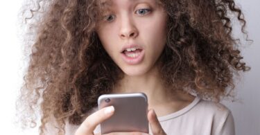 Surprised young woman looking at her phone, checking if online money earning sites are genuine or fake