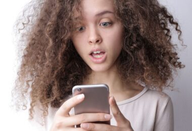 Surprised young woman looking at her phone, checking if online money earning sites are genuine or fake