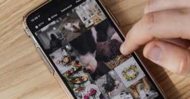 Person scrolling a smartphone photo gallery on a wooden table, saving pictures without an Instagram photo downloader