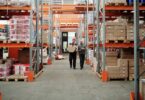 Warehouse workers carrying a package past stocked shelves, illustrating a Wholesale2b dropshipping supplier