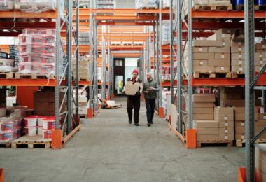 Warehouse workers carrying a package past stocked shelves, illustrating a Wholesale2b dropshipping supplier