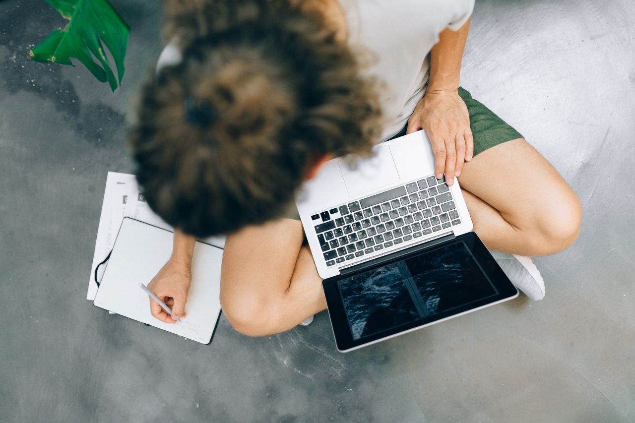 Man writing in a notebook beside his laptop, tracking a beginner online money side project