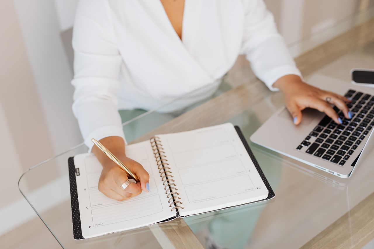 Person planning an email campaign in a notebook while using a laptop, the first step in using AWeber