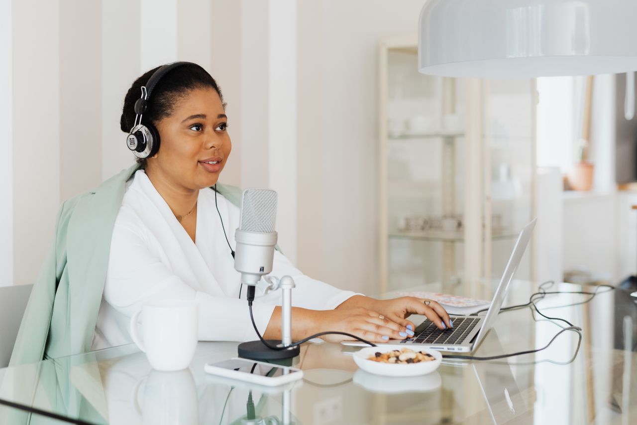 Creator working on a laptop with a microphone in a home studio, planning products to sell on Podia