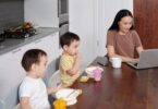 Woman working on her laptop near her kids at breakfast, showing how to make money from home
