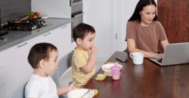 Woman working on her laptop near her kids at breakfast, showing how to make money from home