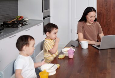Woman working on her laptop near her kids at breakfast, showing how to make money from home