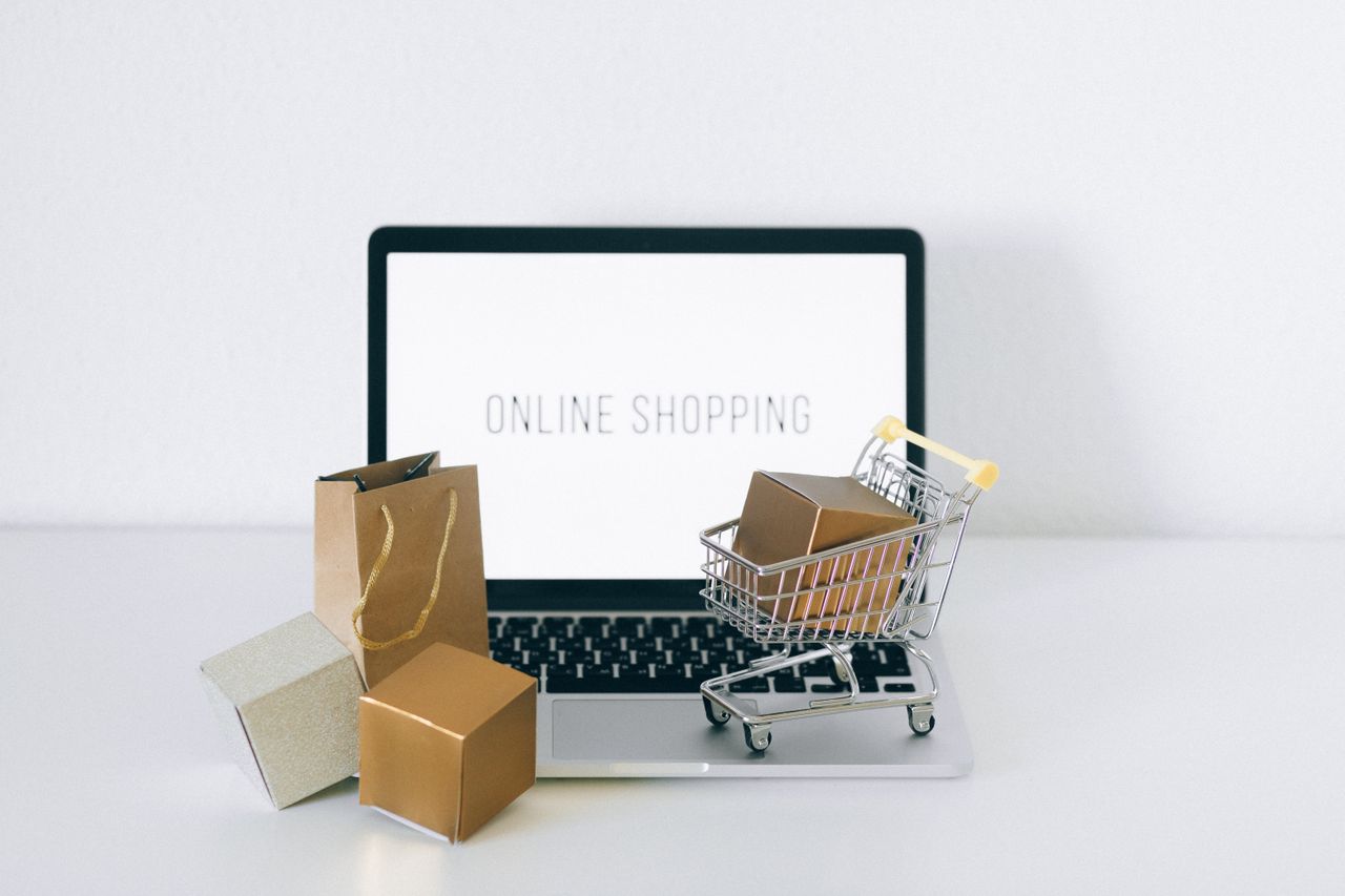 Laptop showing an online shop beside boxes and a mini cart, for moving to Shopio alternatives