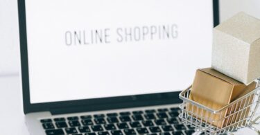 Miniature shopping cart and smartphone on a laptop, representing the best ecommerce website builder for online stores