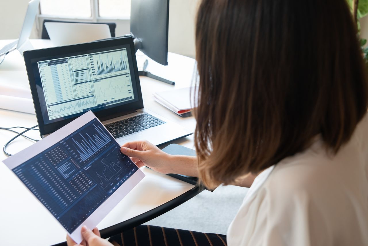 Woman reviewing charts on paper and a laptop while comparing GetResponse pricing plans