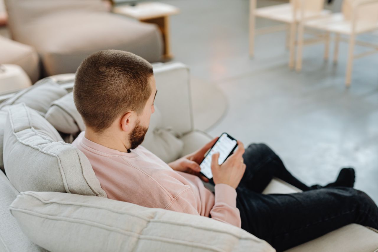 Man on a couch using a smartphone app, the typical way people make money watching ads