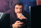 Man in a hoodie using a smartphone among digital screens, illustrating Instadownloader security risks