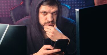 Man in a hoodie using a smartphone among digital screens, illustrating Instadownloader security risks