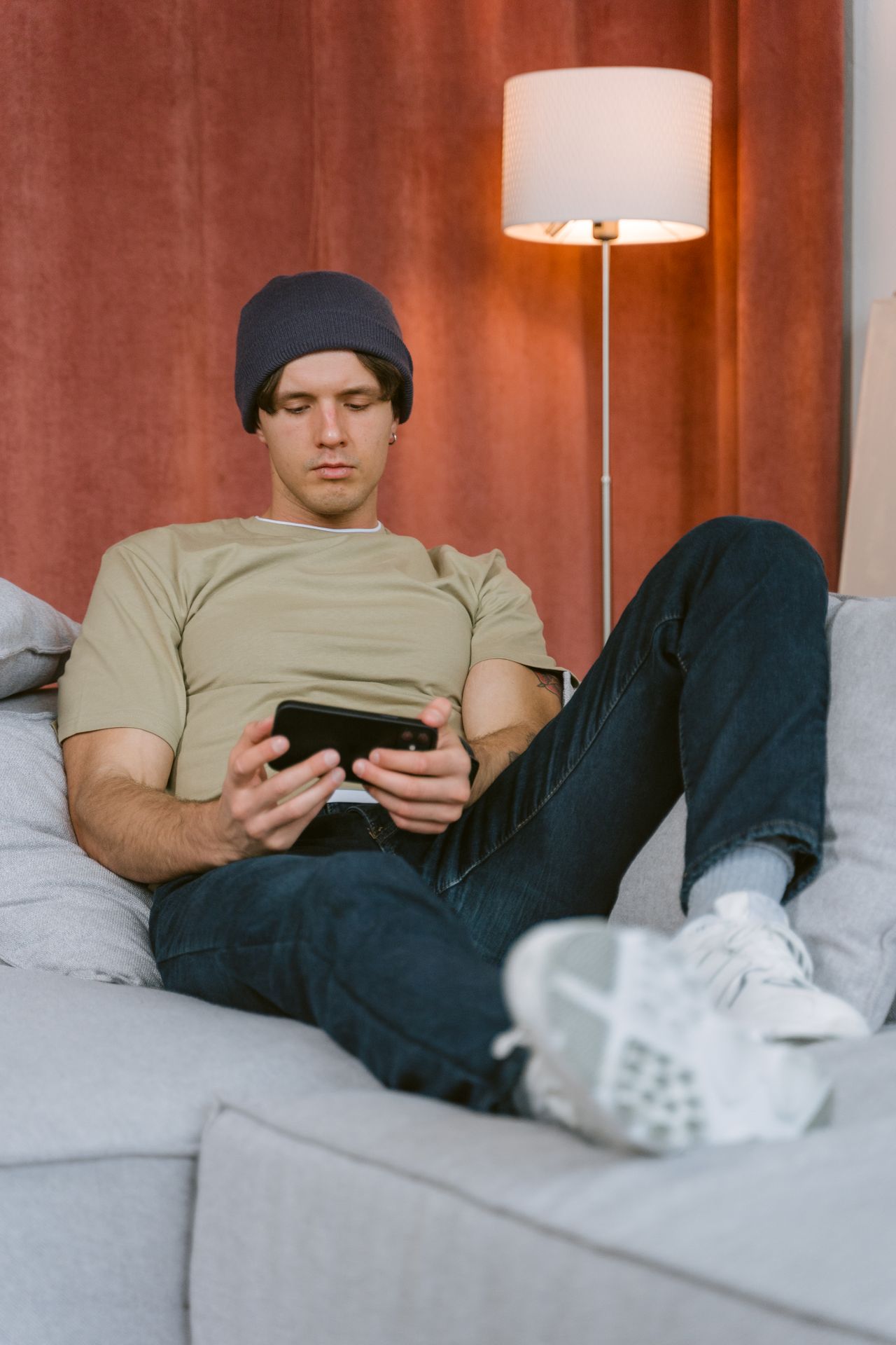 Man on a sofa checking a phone app that pays small amounts of easy money online