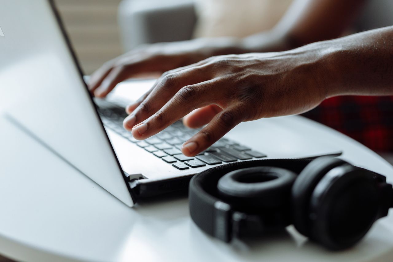 Hands typing on a laptop beside headphones, like transcription work that pays weekly