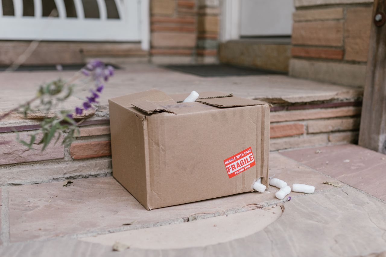 Damaged cardboard box with a fragile sticker on porch steps, a case for a USPS lost or damaged package claim