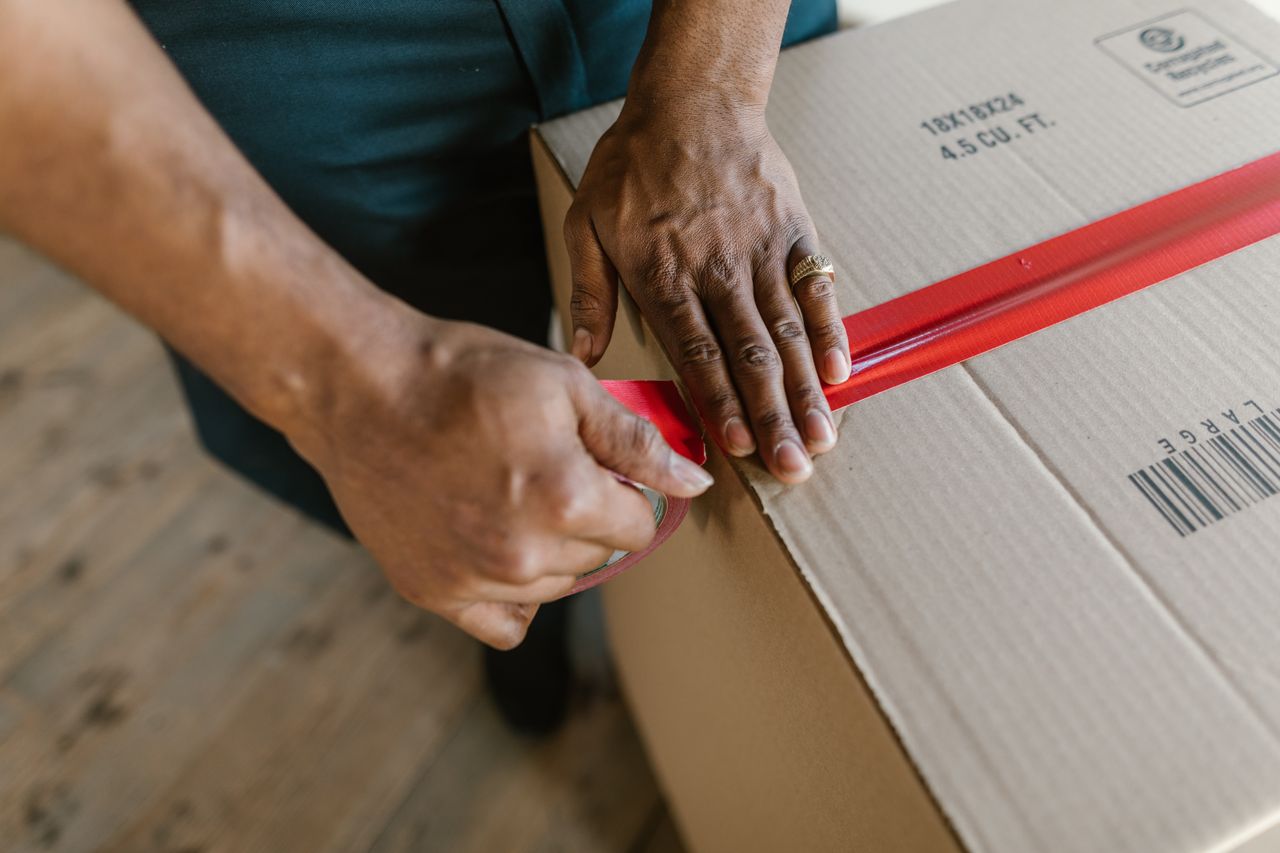 Person taping a cardboard box to ship an item sold on an online money making site