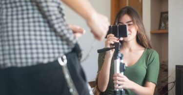 Young woman recording a vlog on a smartphone tripod, creating Reels people try to save with an Instagram video downloader