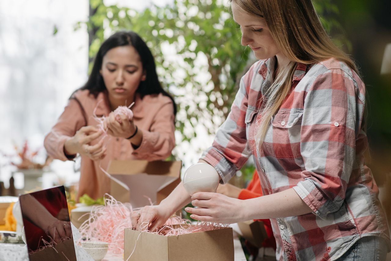 Two women packing customer orders into cardboard boxes, a beginner online selling business
