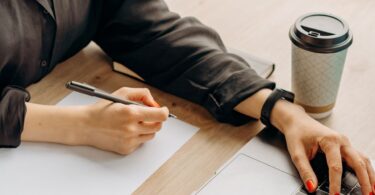 Writer typing on a laptop with pen in hand, working on ways to make money writing online