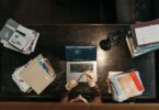 Student at a wooden desk with books and a laptop, searching for online jobs without investment from home
