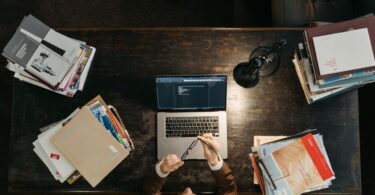 Student at a wooden desk with books and a laptop, searching for online jobs without investment from home